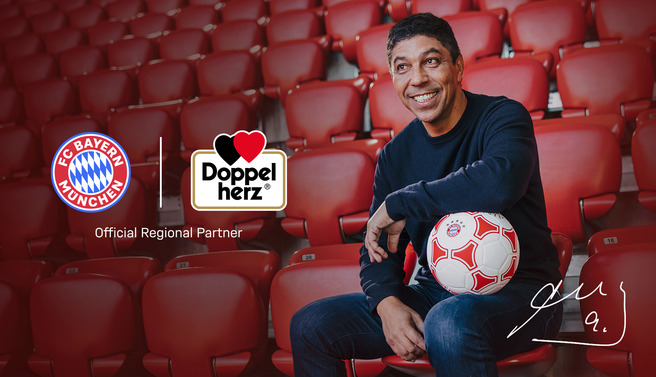 A smiling man sits in a stadium seat holding a soccer ball, with logos of FC Bayern München and Doppelherz nearby. Text indicates that Doppelherz is the official regional partner. The background features empty stadium seating, emphasizing the partnership theme.